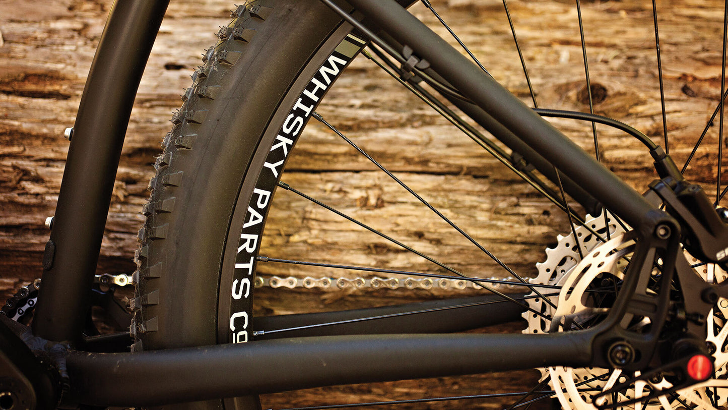 Close-up of a bicycle wheel with 'Whisky Parts Co' branding against a wooden background