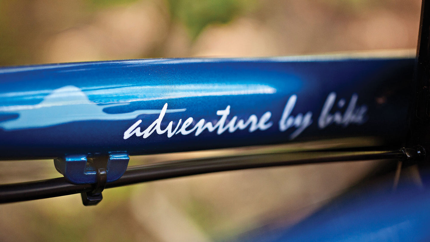 Close-up of a blue bicycle frame with 'adventure by bike' branding.
