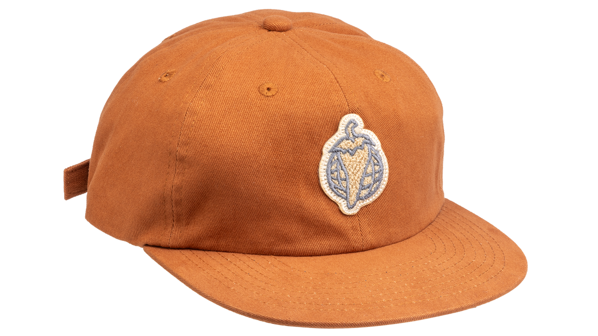 A rust-orange cotton flat-brim cap featuring a small embroidered patch of a pepper on the front