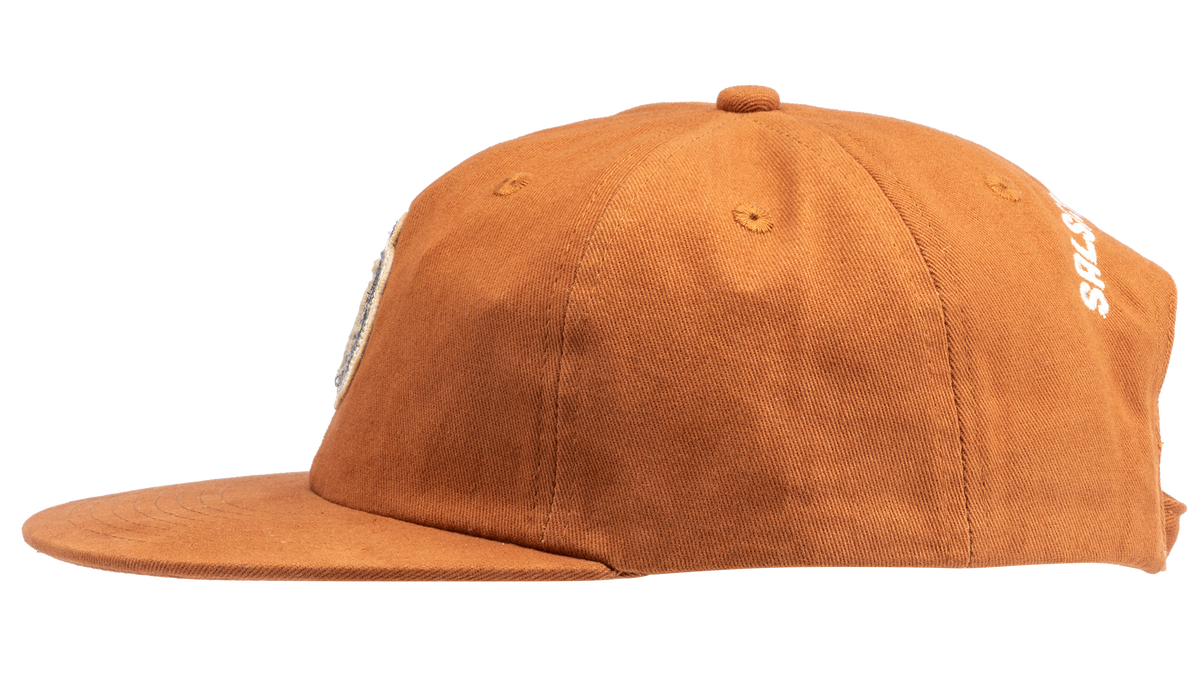 A rust-orange cotton flat-brim cap featuring a small embroidered patch of a pepper on the front - side view