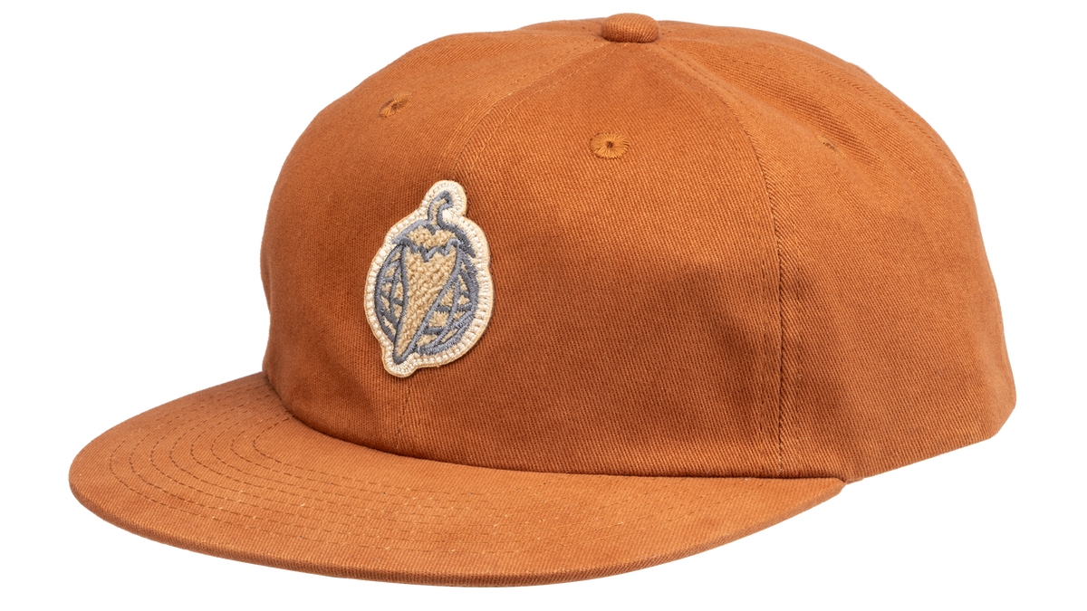 A rust-orange cotton flat-brim cap featuring a small embroidered patch of a pepper on the front