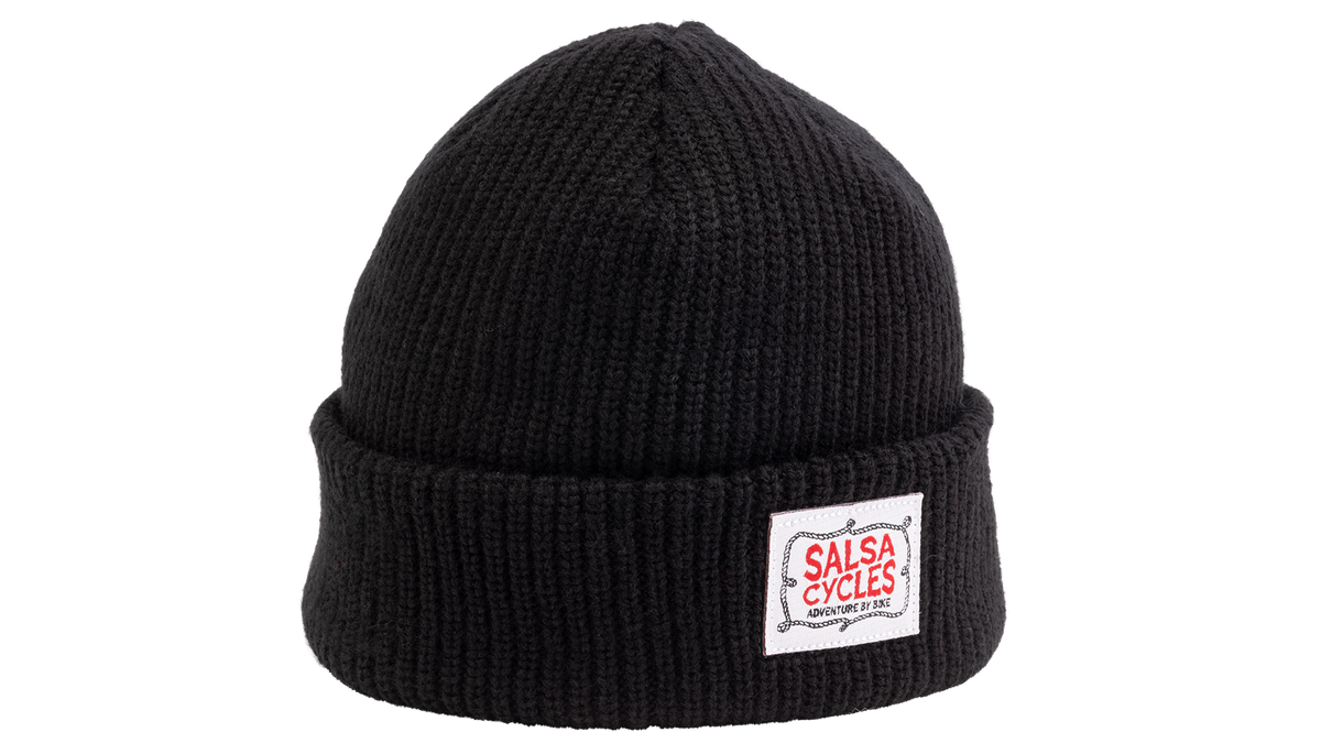 A black ribbed knit beanie hat with a folded cuff, featuring a white rectangular patch on the front with the red and white 'SALSA CYCLES' logo.
