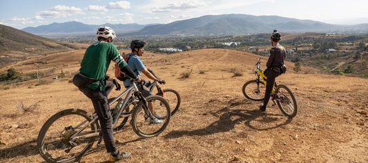 Three mountain bikers taking a break, on hillside looking down at city in the valley, mountains in distance