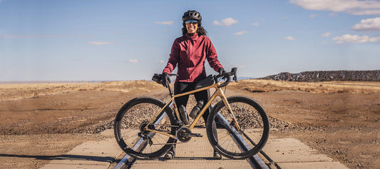 Front view of a smiling cyclist, standing across railroad track behind a Salsa Warbird bike in the rocky tundra