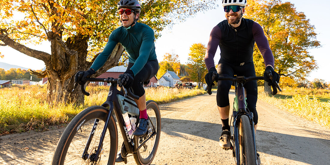 Two cyclists riding their Salsa Flyway gravel bikes on a dirt road with autumn trees in the background