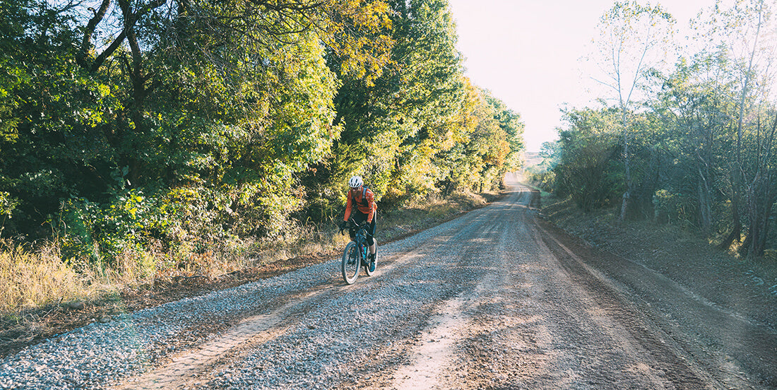 Cyclist riding a Salsa Flyway gravel bike on a gravel road surrounded by trees