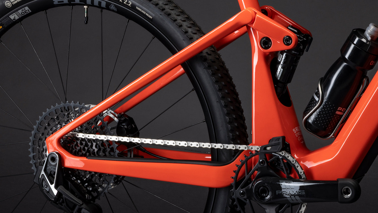 Close-up of an orange bicycle frame with chain and gear on a black background