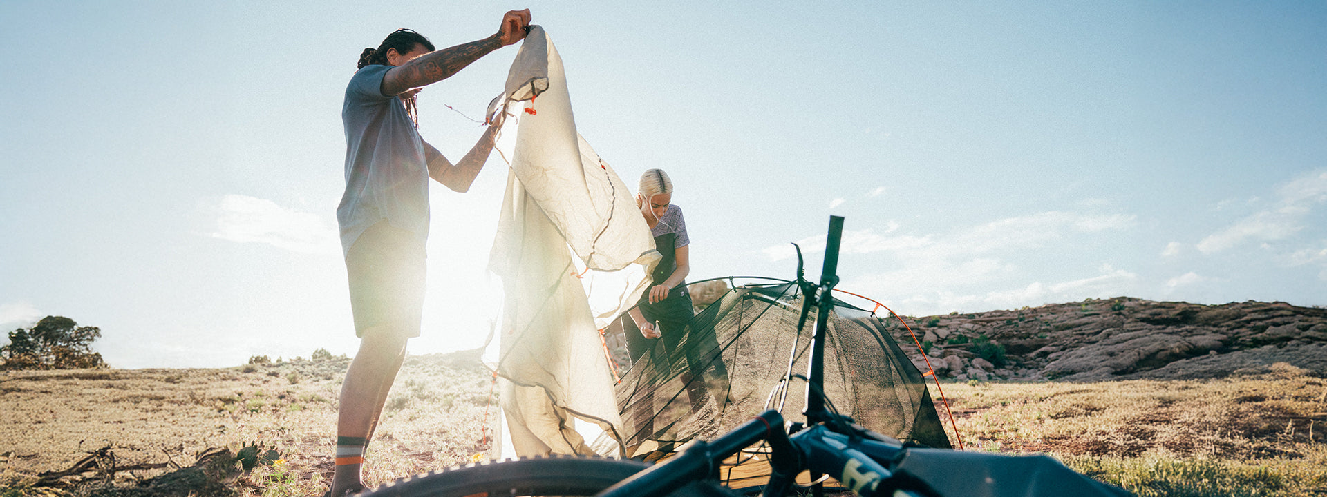 Two people setting up a tent in a field with a clear sky