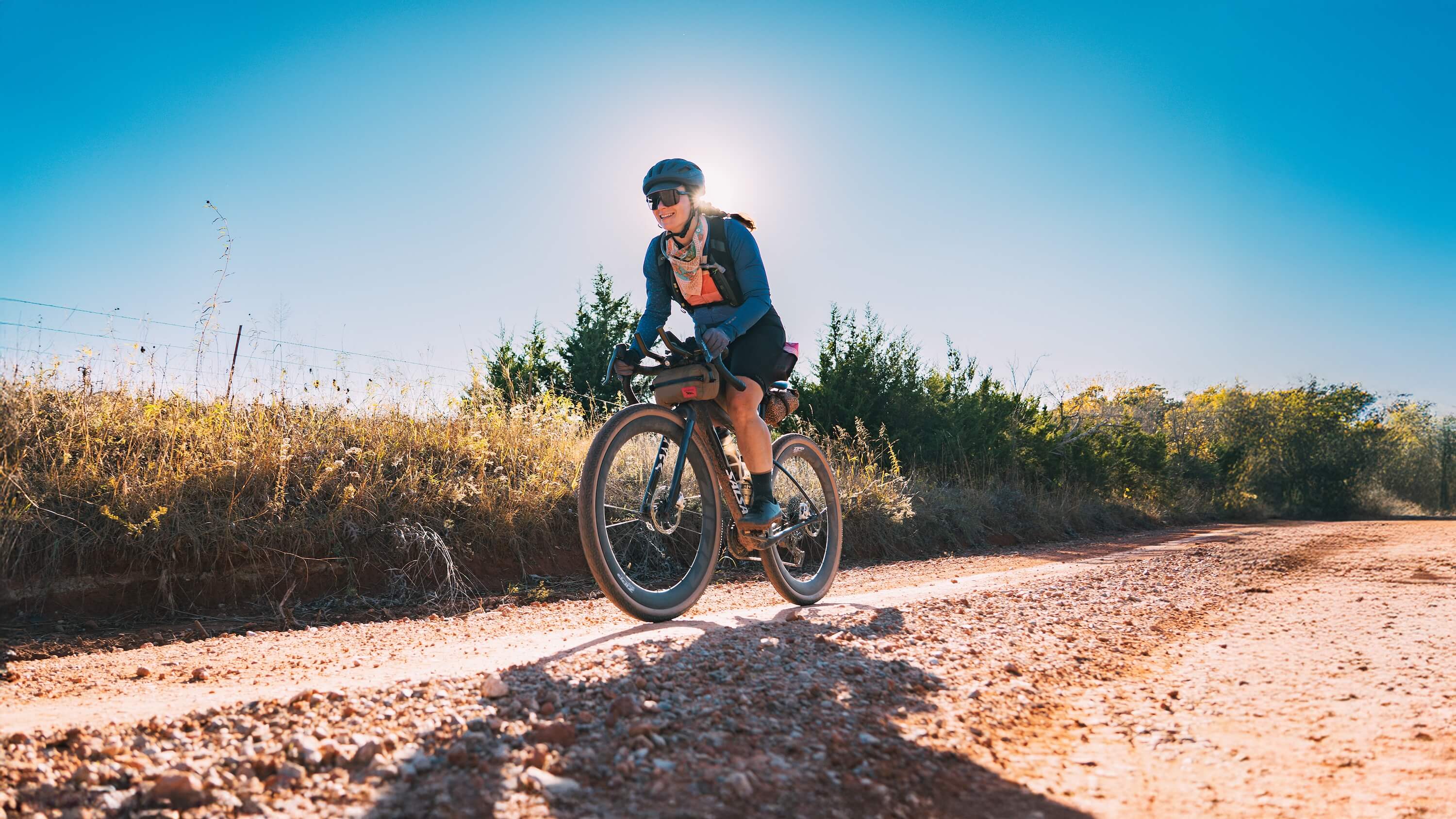 Cyclist riding a Salsa Flyway gravel bike on a dirt road with a clear blue sky