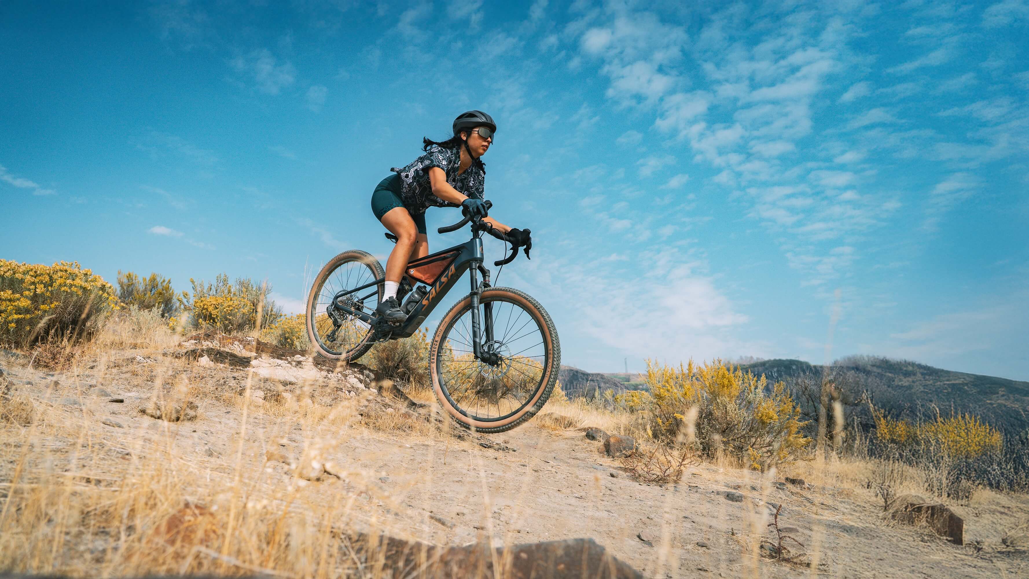 Person riding a Salsa Wanderosa ebike down a rocky trail with a clear blue sky