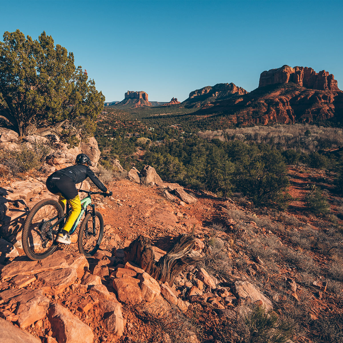 Person mountain biking on rocky terrain with desert landscape and red rock formations in the background