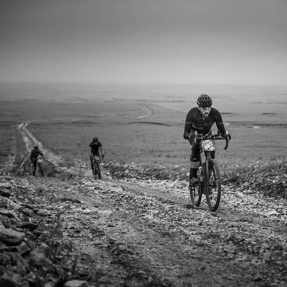 Three gravel cyclists on a dirt trail with a vast landscape in the background