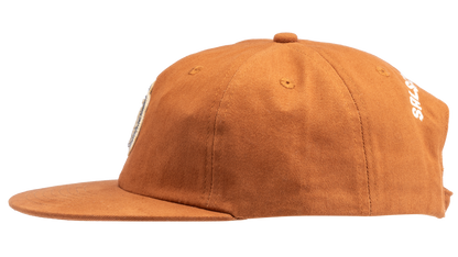 A rust-orange cotton flat-brim cap featuring a small embroidered patch of a pepper on the front -  side view