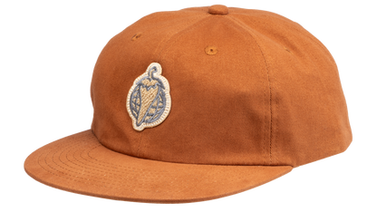 A rust-orange cotton flat-brim cap featuring a small embroidered patch of a pepper on the front