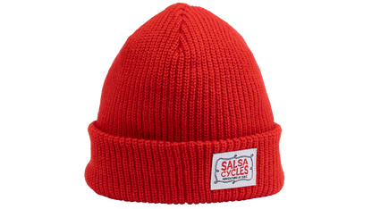 A bright red ribbed knit beanie hat with a folded cuff, featuring a white rectangular patch on the front that reads 'SALSA CYCLES' 