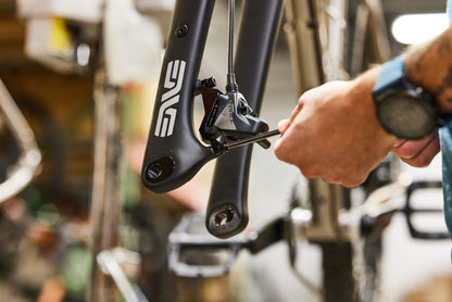 Person adjusting a bicycle component with a brand logo in a workshop setting